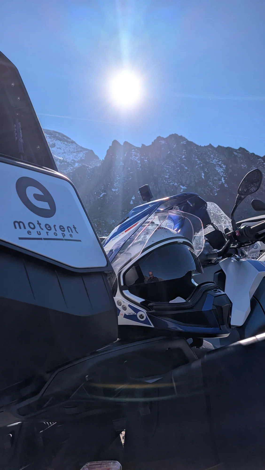 Casco y maleta MotoRent frente a montañas